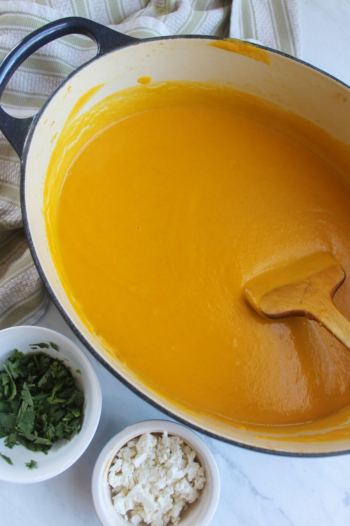 A finished pureed pot of carrot ginger chickpea soup with small bowls of feta and cilantro.