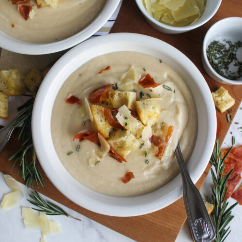 Creamy cauliflower white bean soup with fresh rosemary sprigs and topped with croutons and crispy prosciutto.