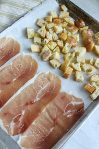 A sheet pan with prosciutto and baguette cubed for croutons.