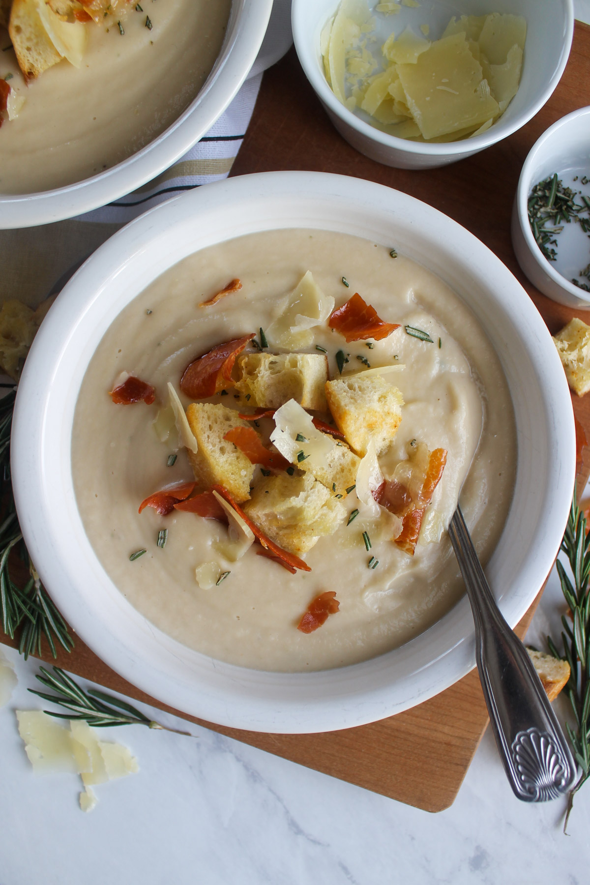 A bowl of cauliflower white bean soup topped with crispy prosciutto, croutons and shaved Parmesan cheese.