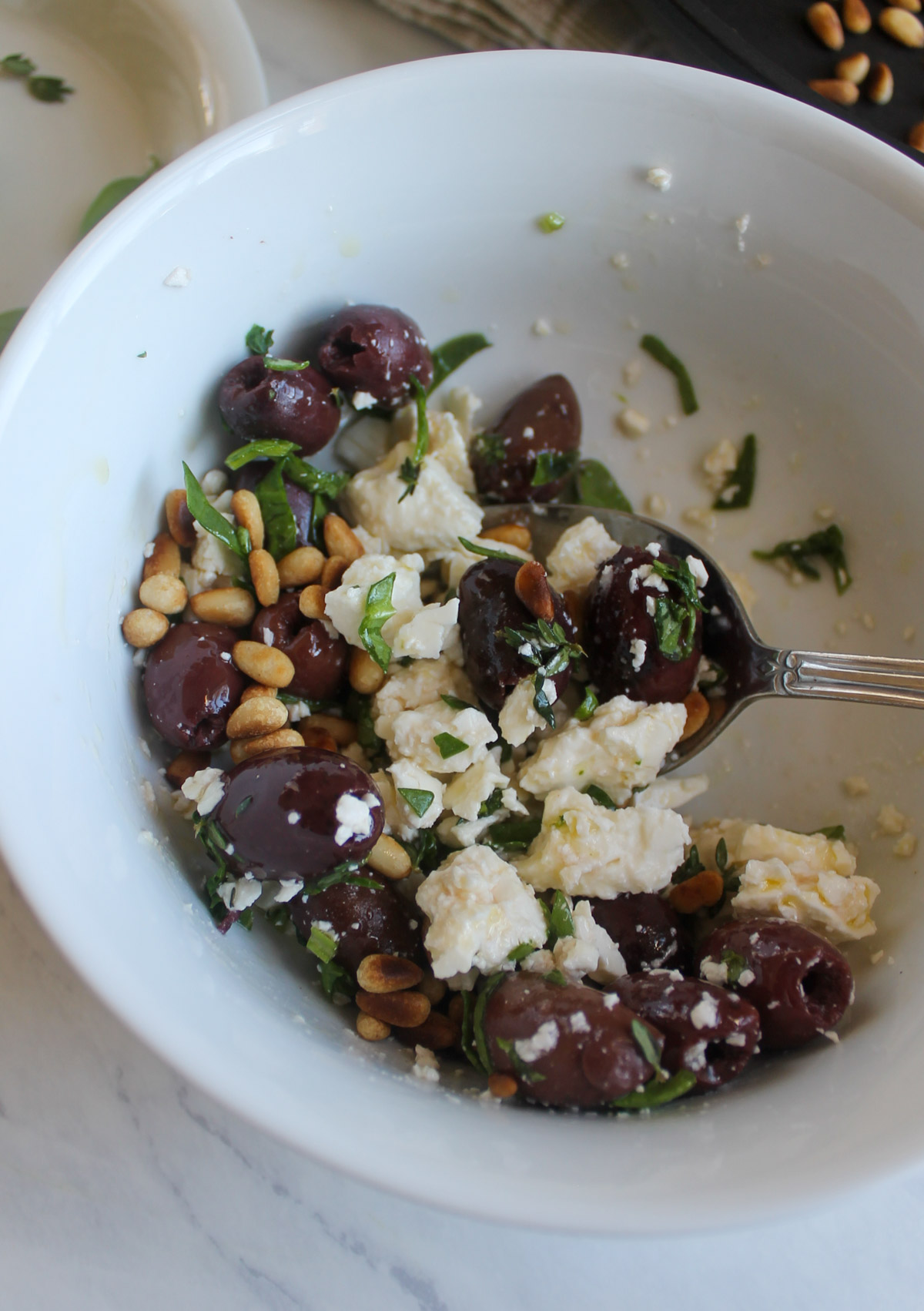 A bowl of hummus topping made of kalamata olives, feta cheese, pine nuts and fresh herbs.