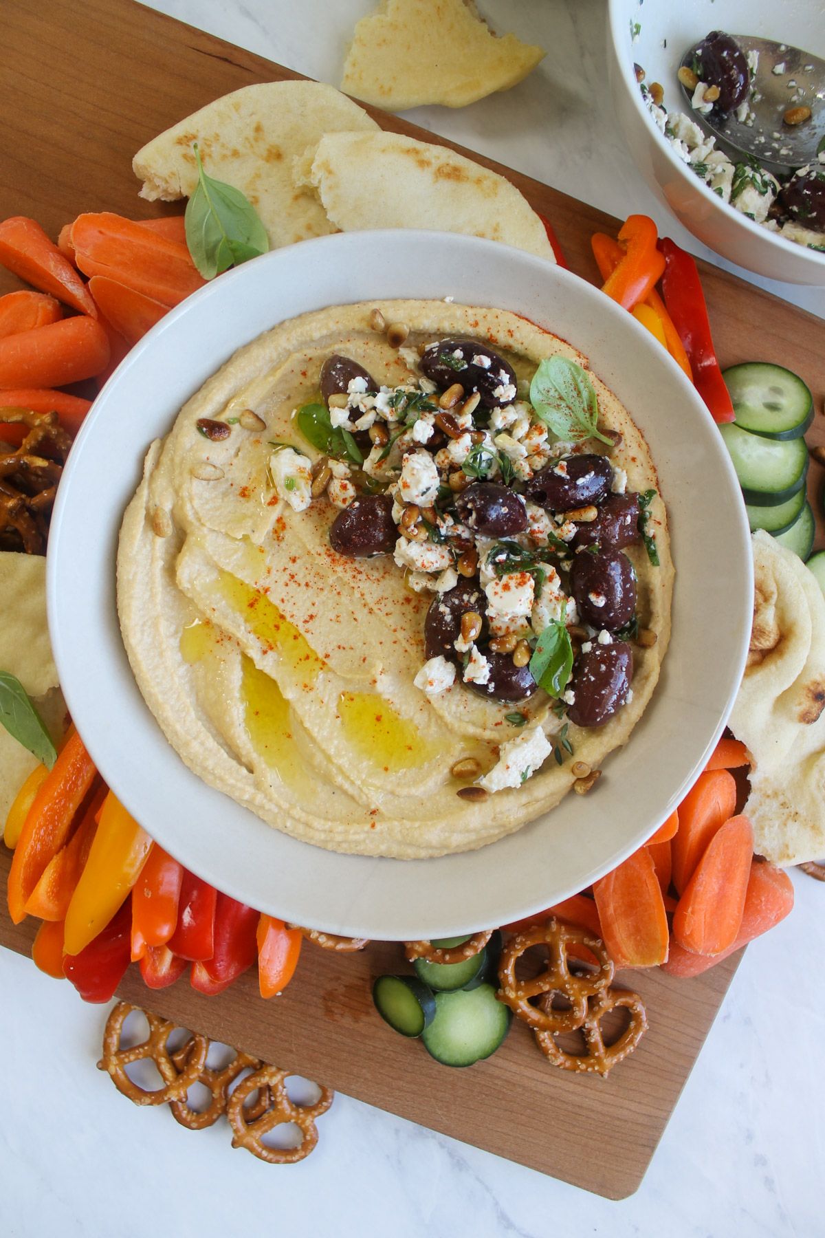 A board of veggies and pita surrounding hummus with feta and olives.