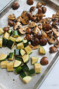 Zucchini and mushrooms tossed on a sheet pan ready to roast.