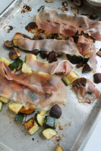 Laying prosciutto over the par roasted vegetables to crisp in the oven.
