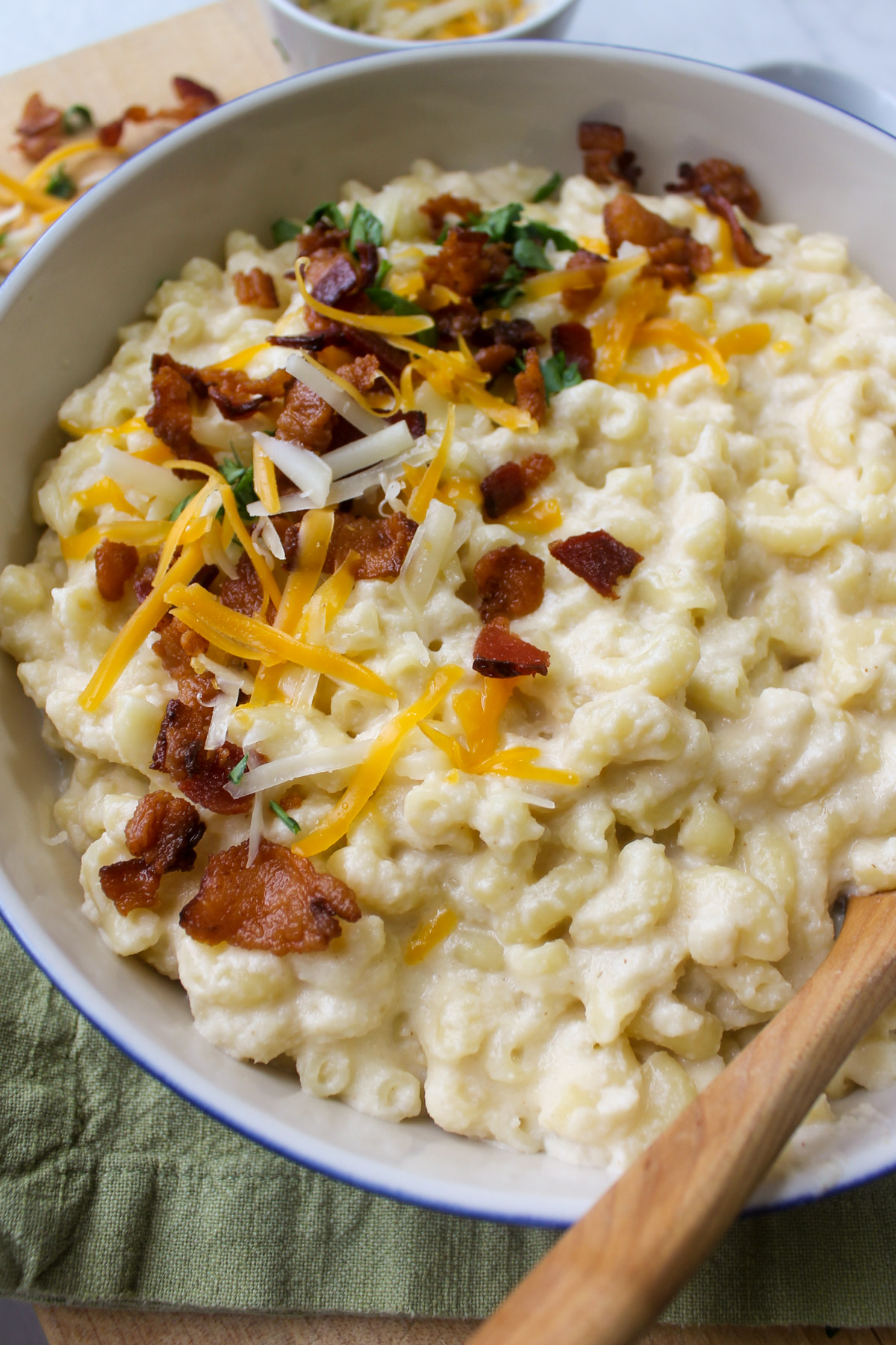 A bowl of bacon cauliflower mac and cheese with a wooden spoon.