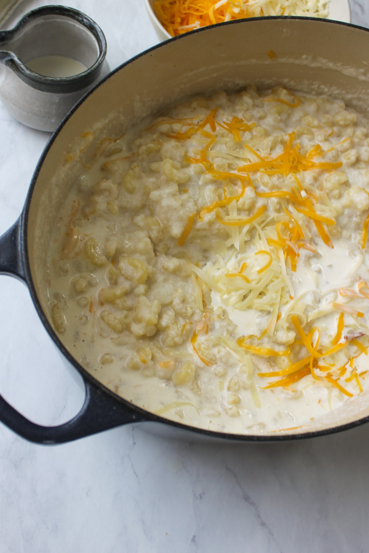 Adding cream and cheese to the bacon cauliflower mac and cheese to form the sauce.