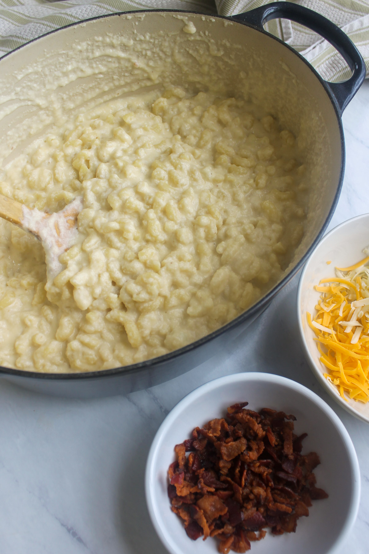 A creamy pot of bacon cauliflower mac and cheese with a bowl of crispy bacon and shredded cheese to add.