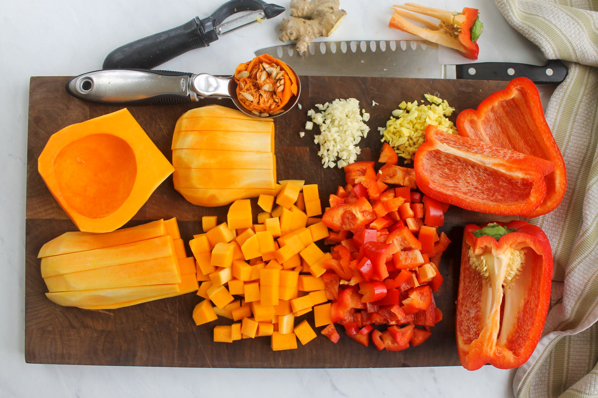 A cutting board with chopped butternut squash, red bell peppers and minced garlic and ginger.