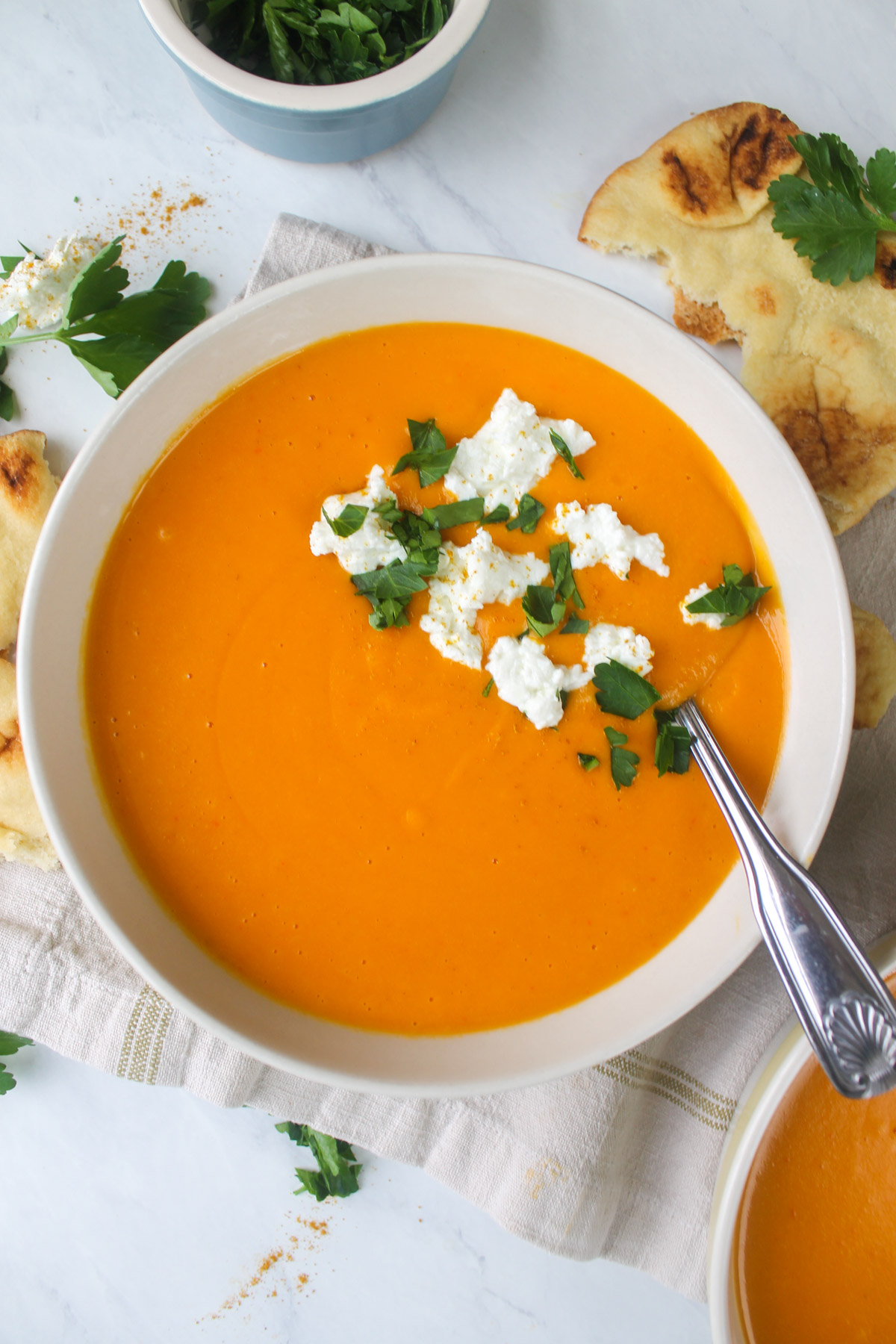 A white bowl of orange pureed soup made from butternut squash and red bell peppers.