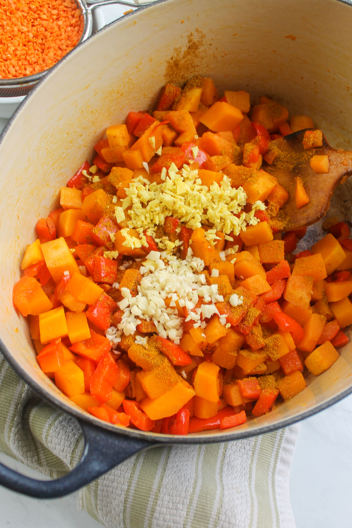 Garlic and ginger being added to butternut squash and red peppers sauteed in a large soup pot.