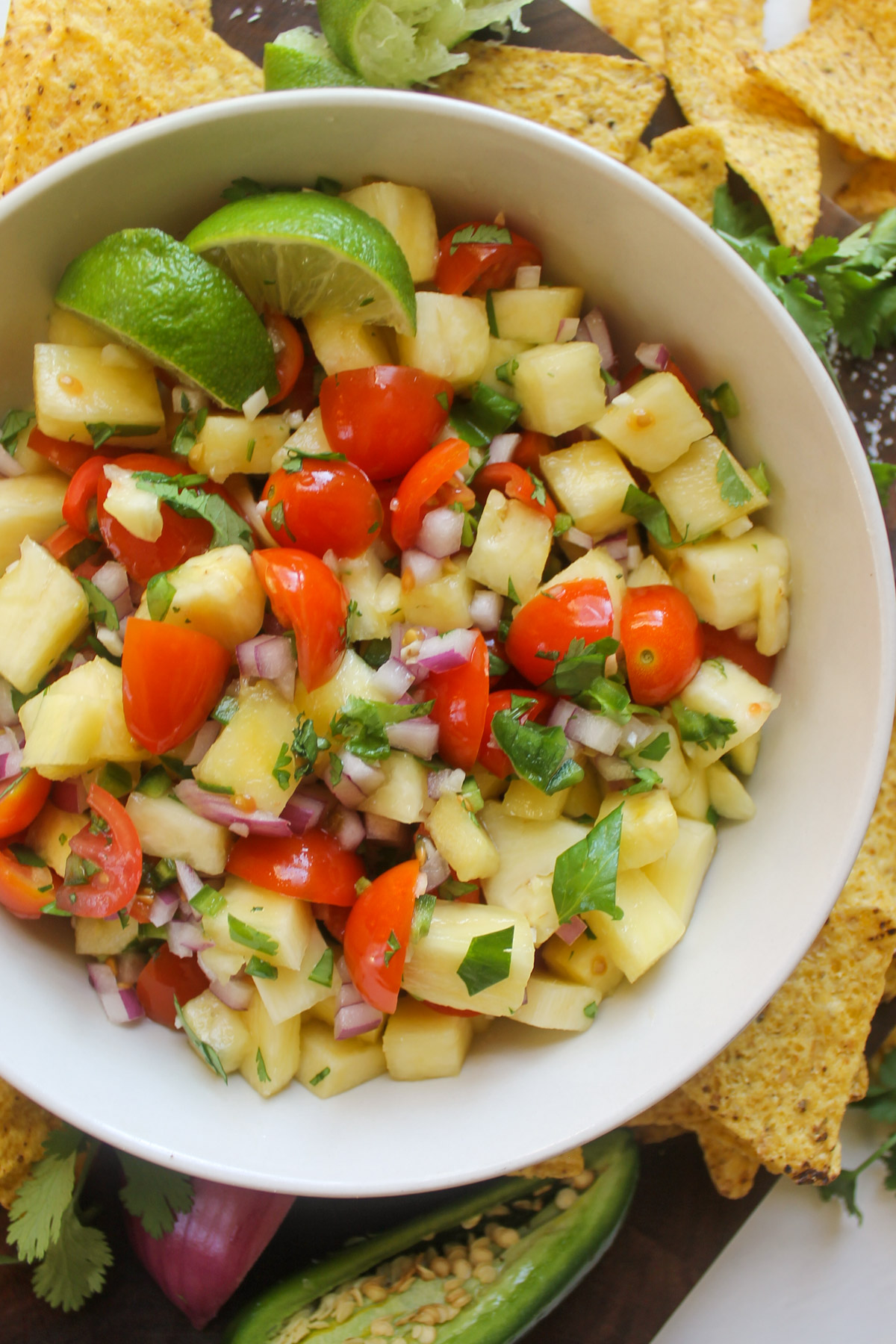 A serving bowl of pineapple pico de gallo with cherry tomatoes and tortilla chips.
