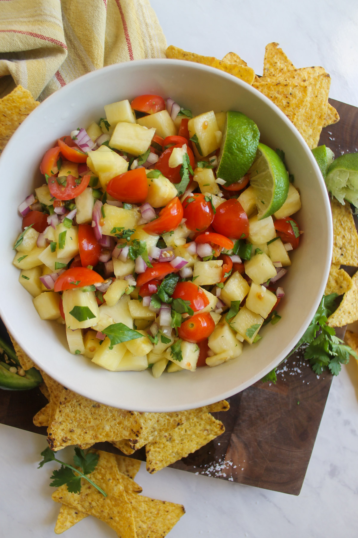 A bowl of pineapple pico de gallo with tortilla chips and lime wedges.