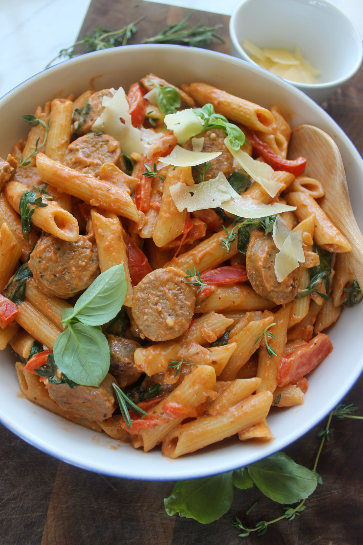 A serving bowl of creamy pink pasta sauce with penne and Italian sausage.