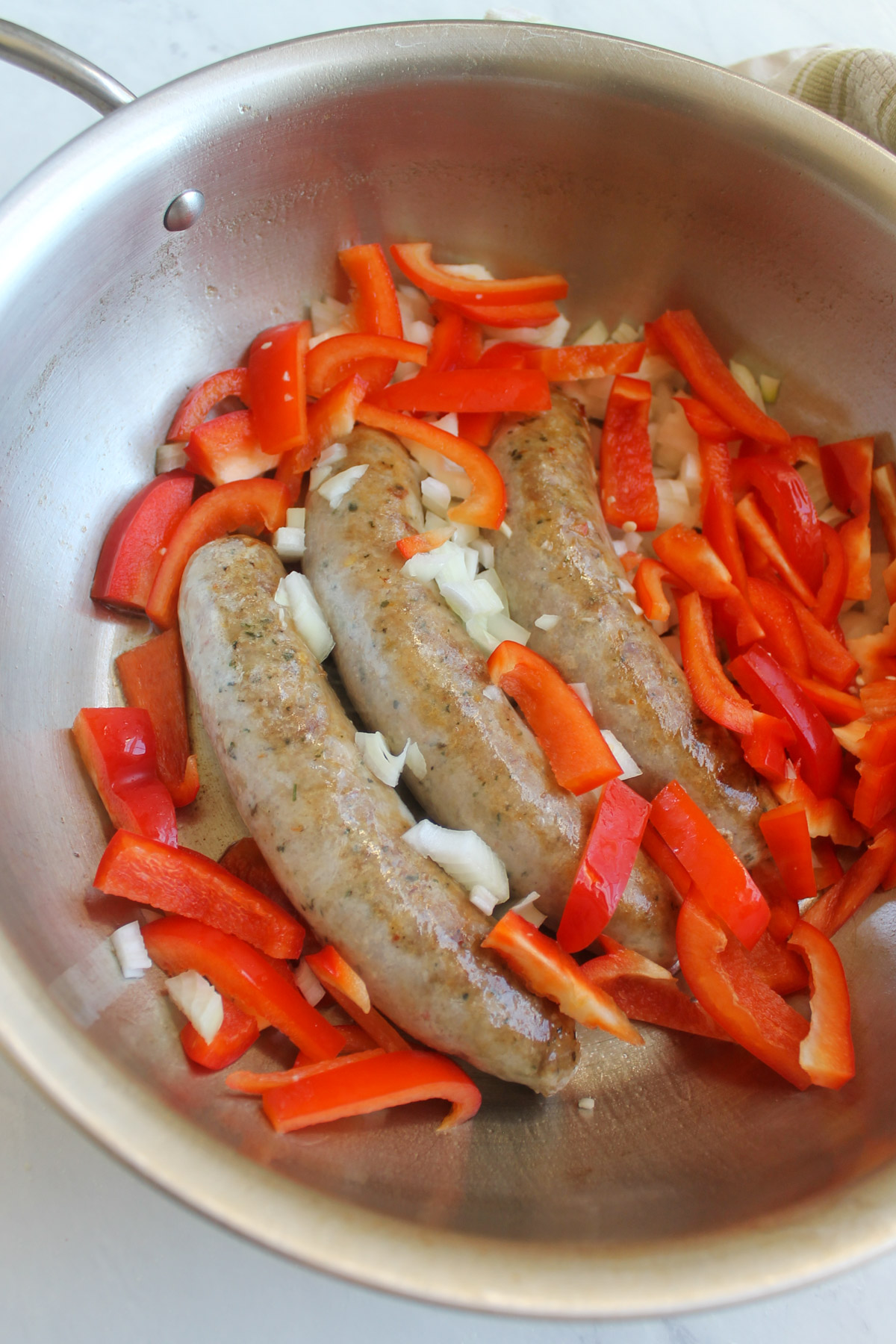 The red bell pepper and onion added to the skillet with the browning Italian sausage links.