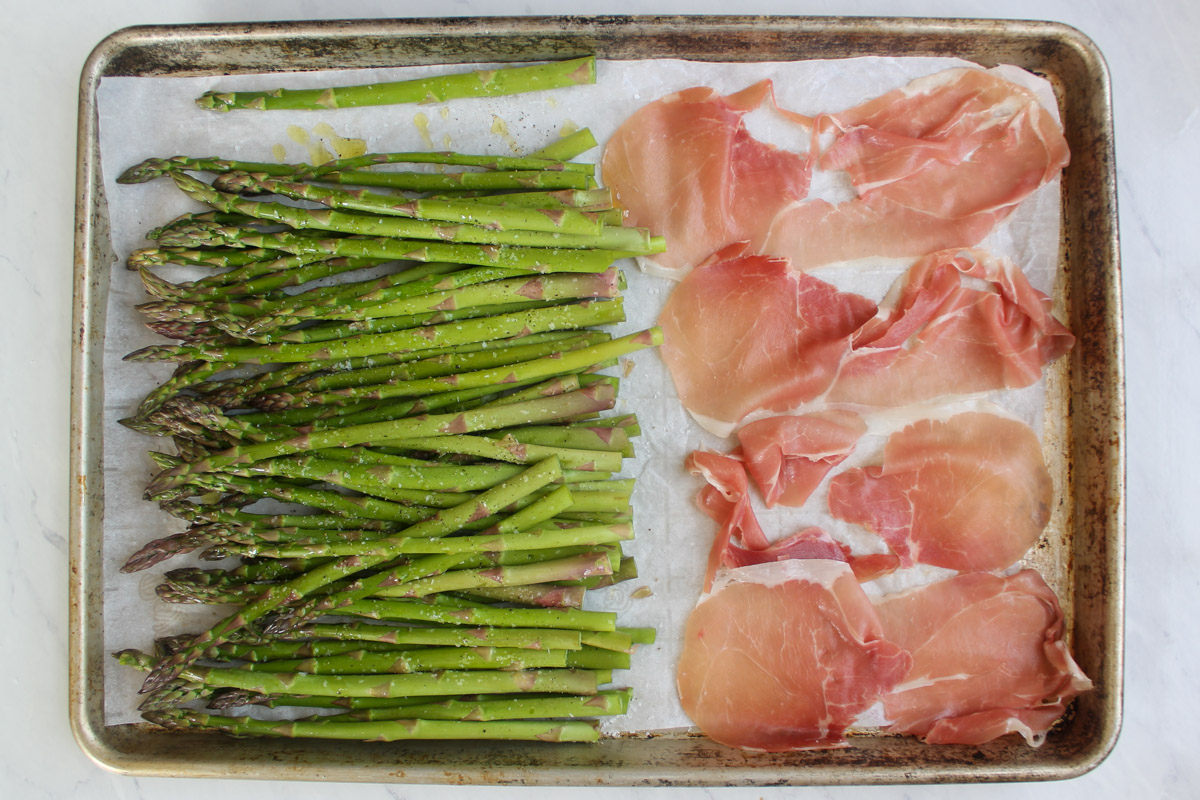 A sheet pan with asparagus on half and prosciutto slices on the other half.