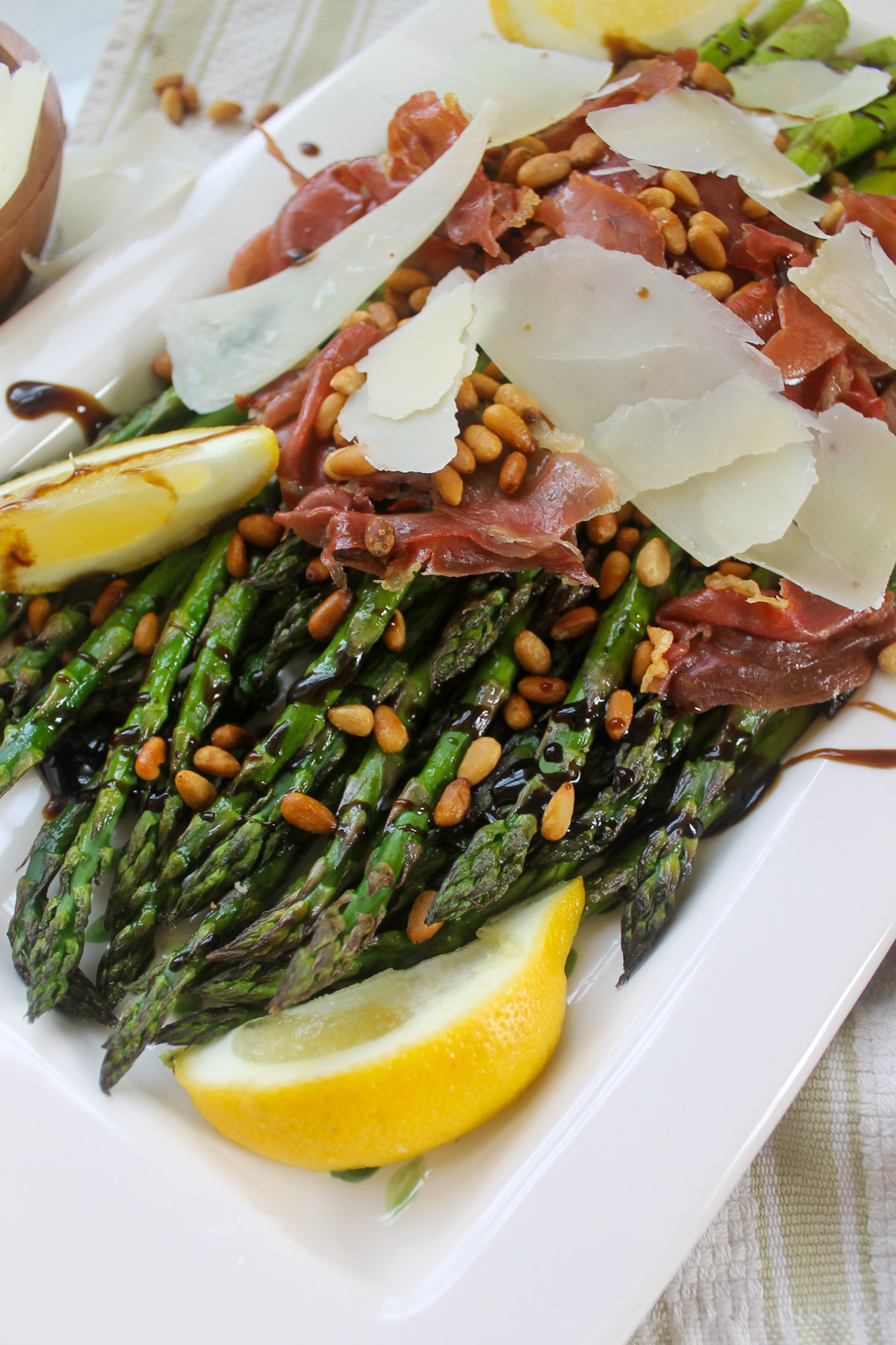A platter of balsamic glazed asparagus with lemon wedges, crispy prosciutto and pine nuts.