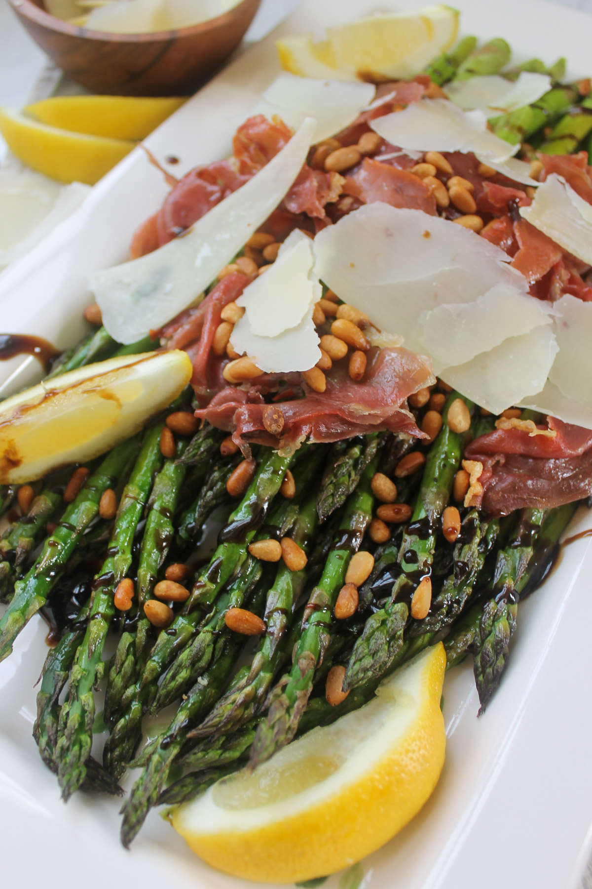 A serving dish of roasted asparagus with crispy prosciutto and big shavings of Parmesan cheese.
