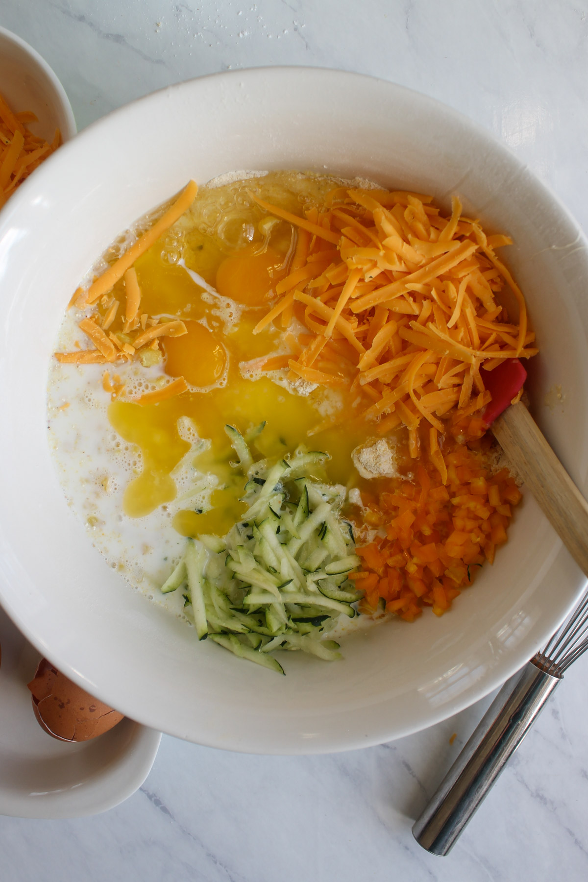 A mixing bowl with all ingredients for skillet cornbread with veggies and cheese.