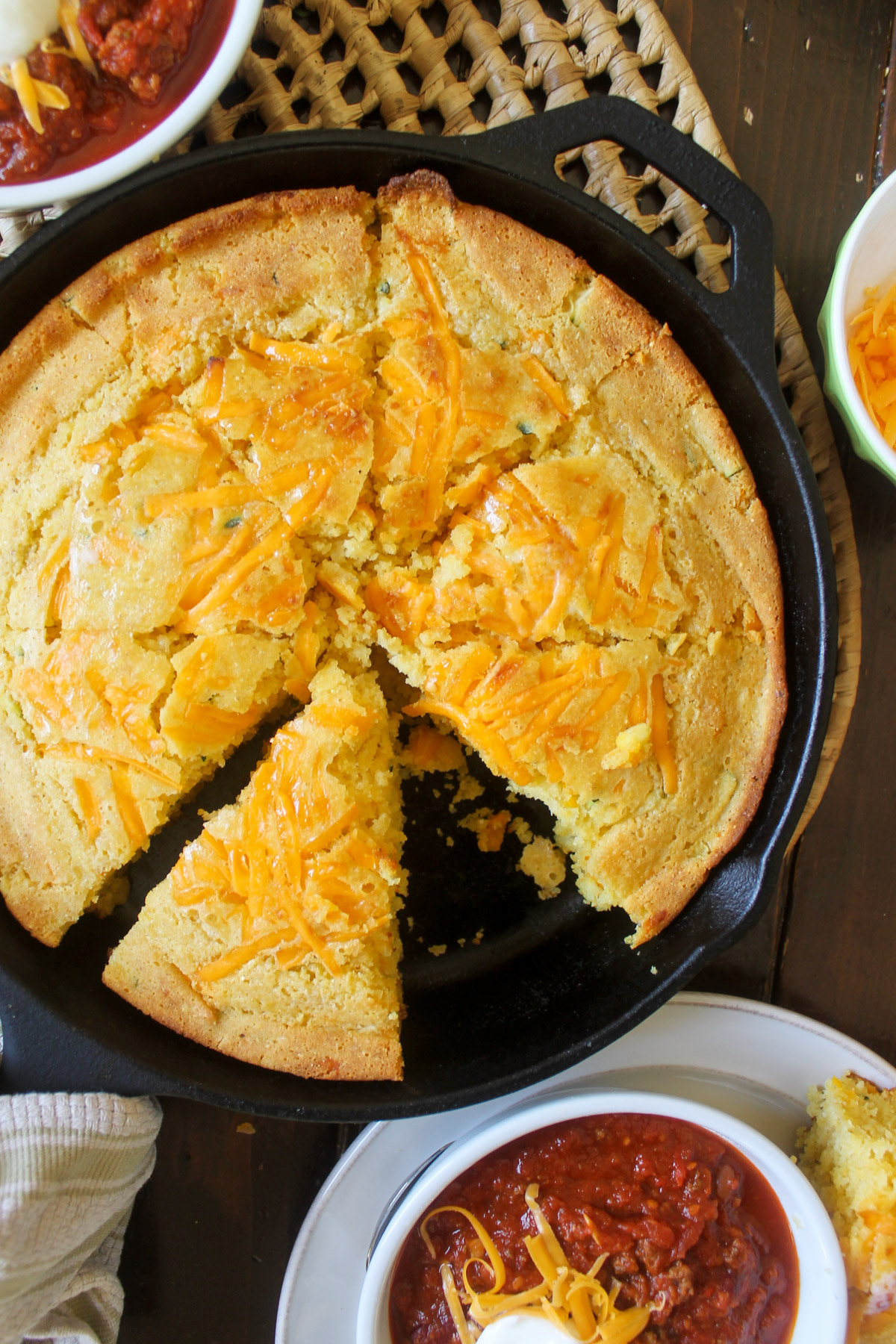 A cast iron skillet of cornbread surrounded by bowls of chili.