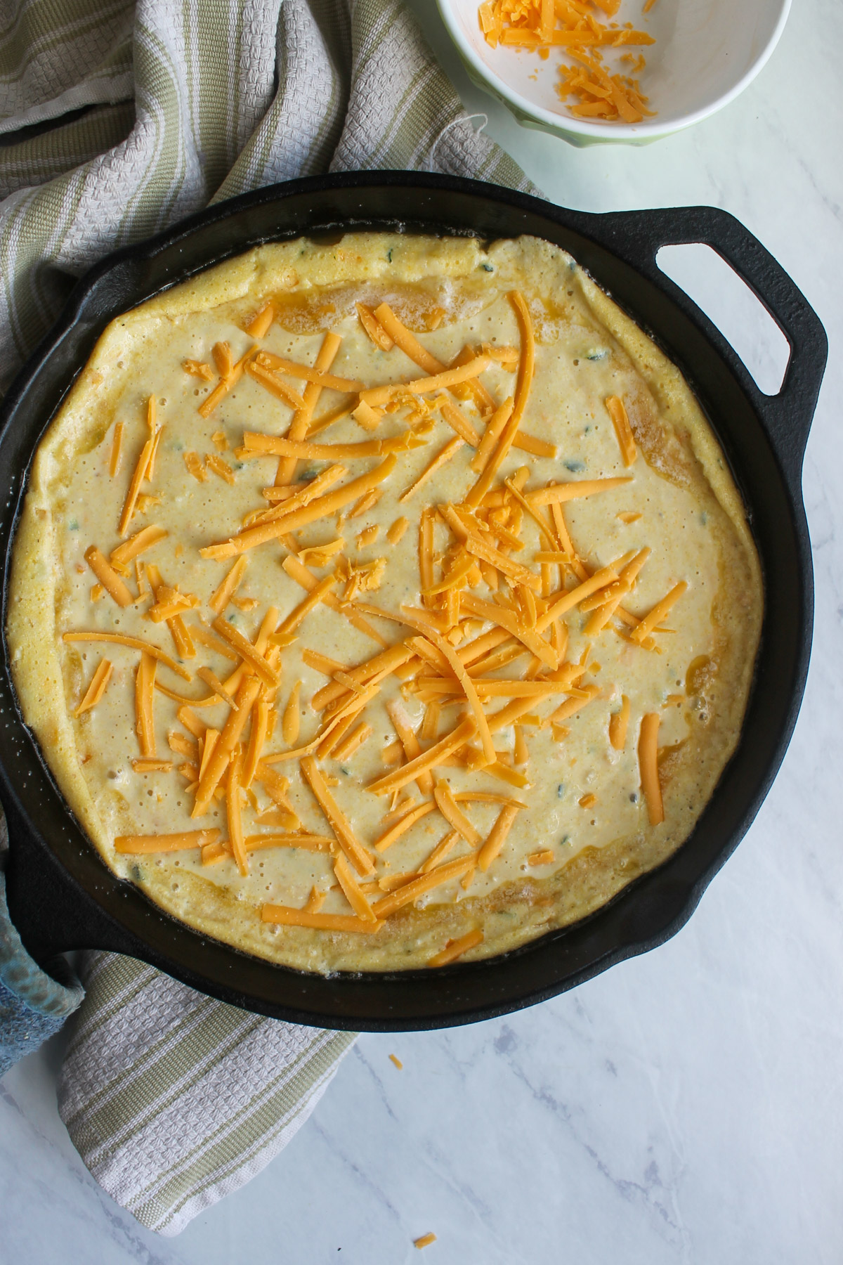 Adding the cornbread batter to the hot skillet and topping with shredded cheese.