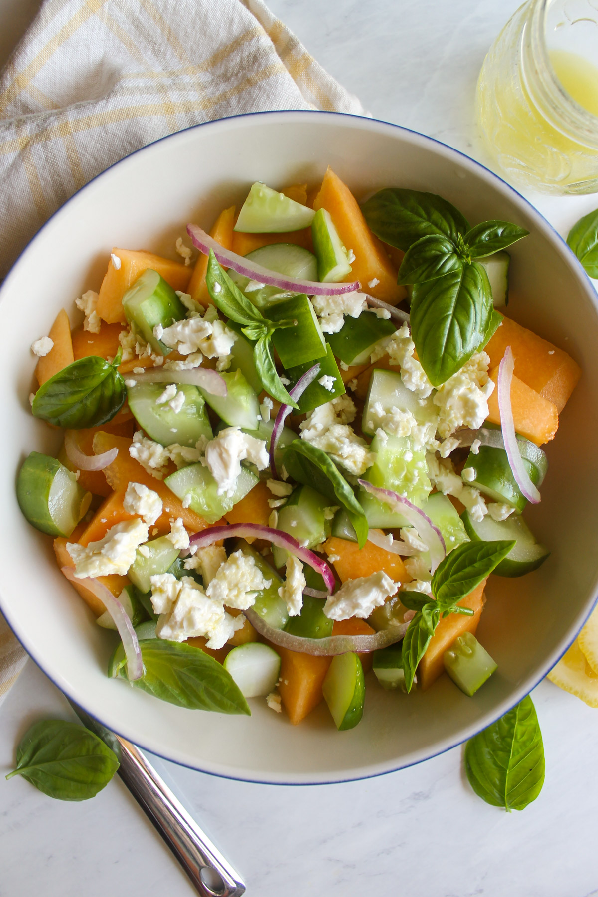 A white bowl of Cucumber Melon Salad with basil leaves.