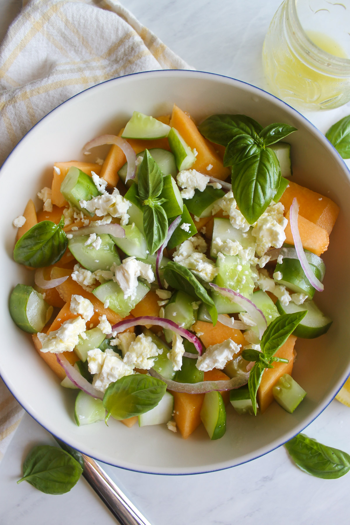 A bowl of Cucumber Melon Salad with feta cheese and red onion slices.
