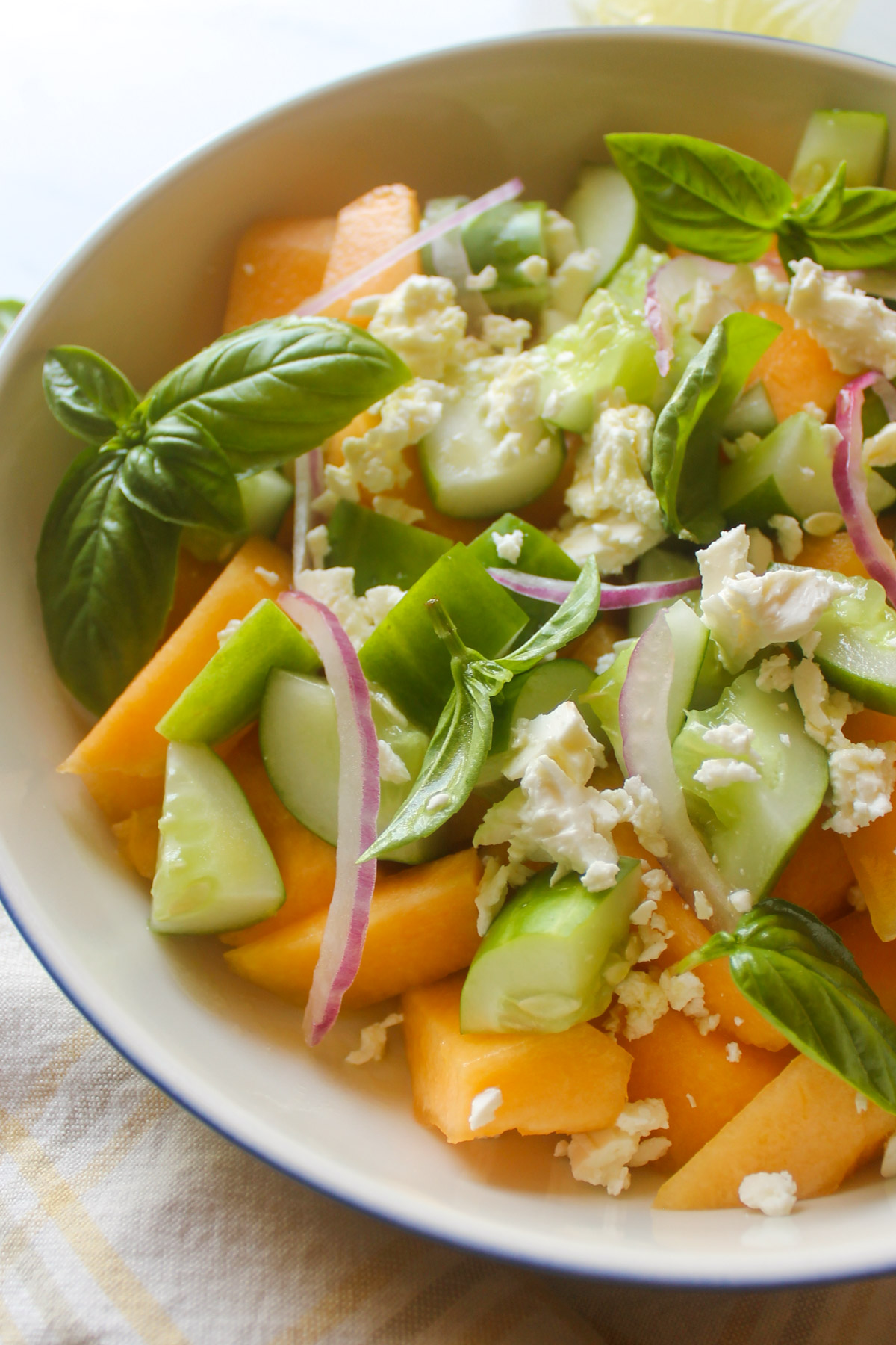 A close up of the bowl of Cucumber Cantaloupe Salad with fresh basil leaves.