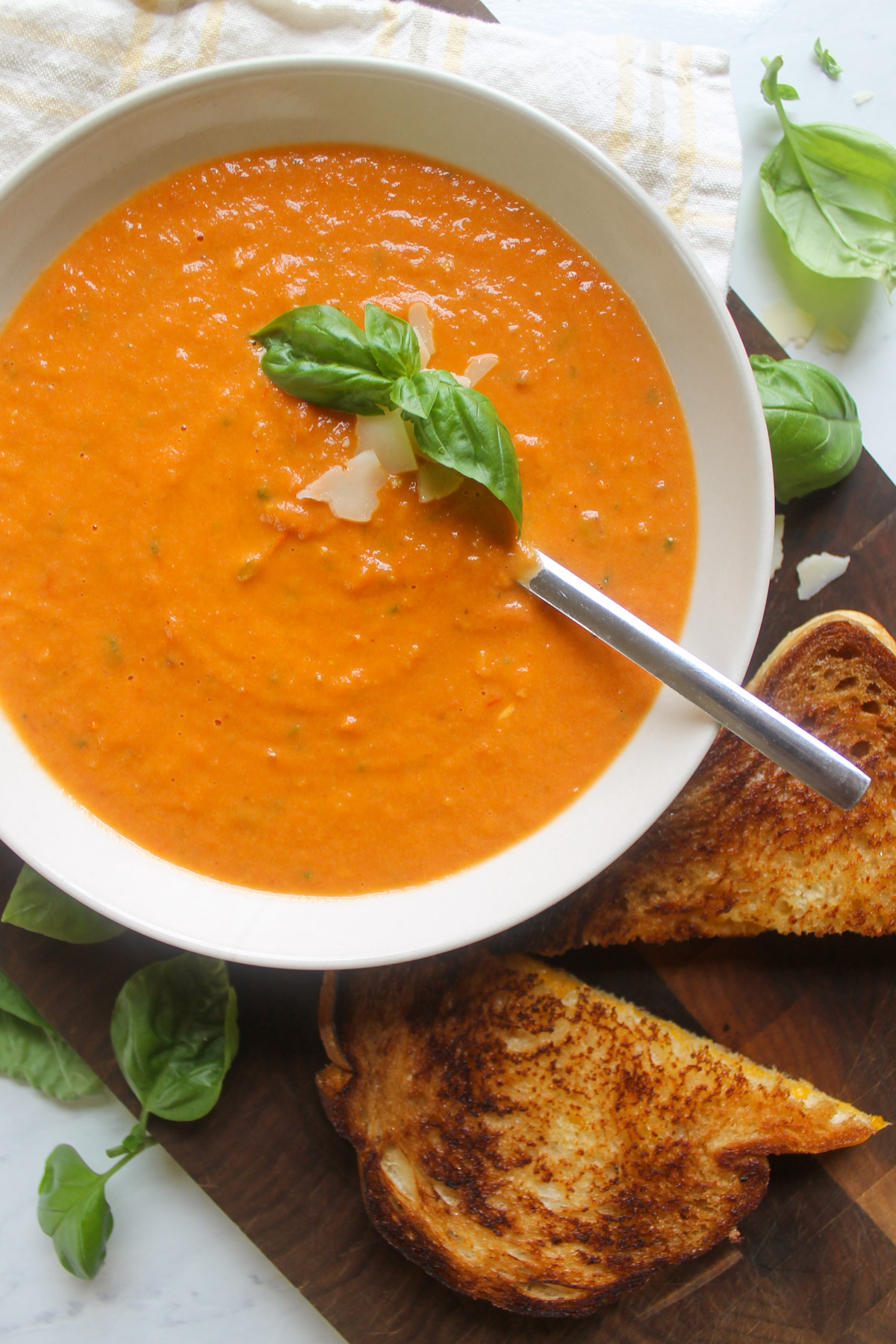 A bowl of garden tomato soup on a dark wooden cutting board with grilled cheese triangles.
