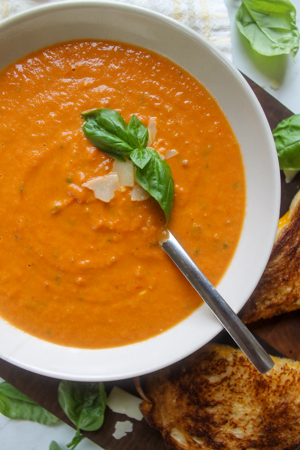 A white bowl of roasted tomato soup with basil.