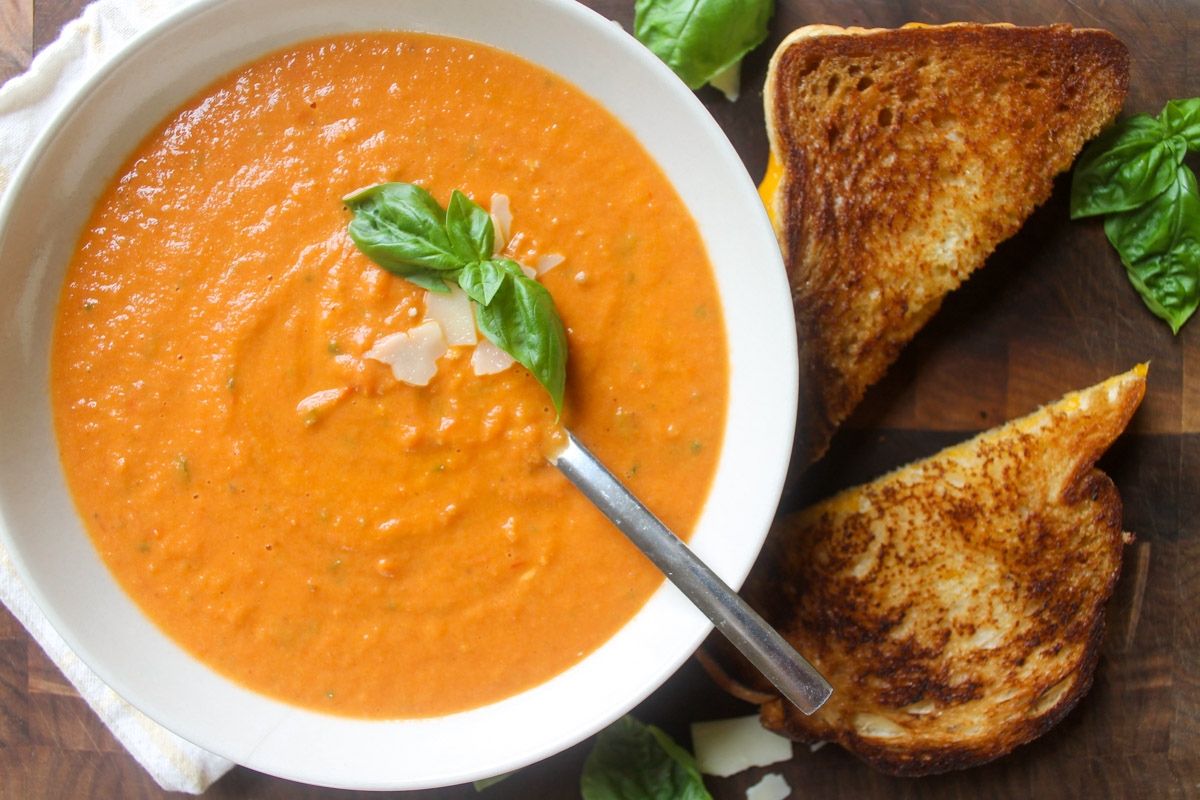 Roasted tomato and garlic soup on a cutting board with grilled cheese.