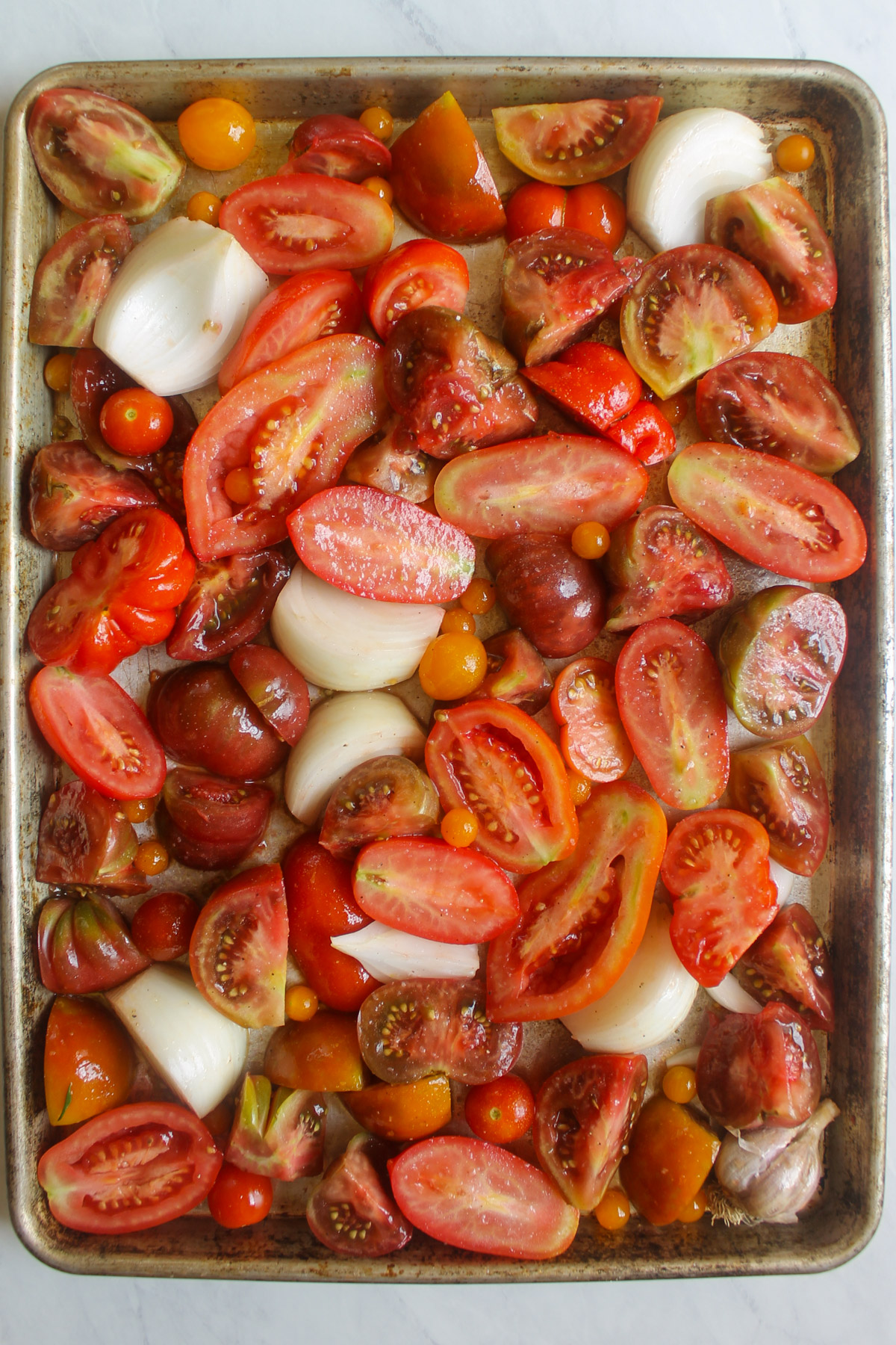 A sheet pan of raw tomatoes cut in pieces with onion and garlic to roast.