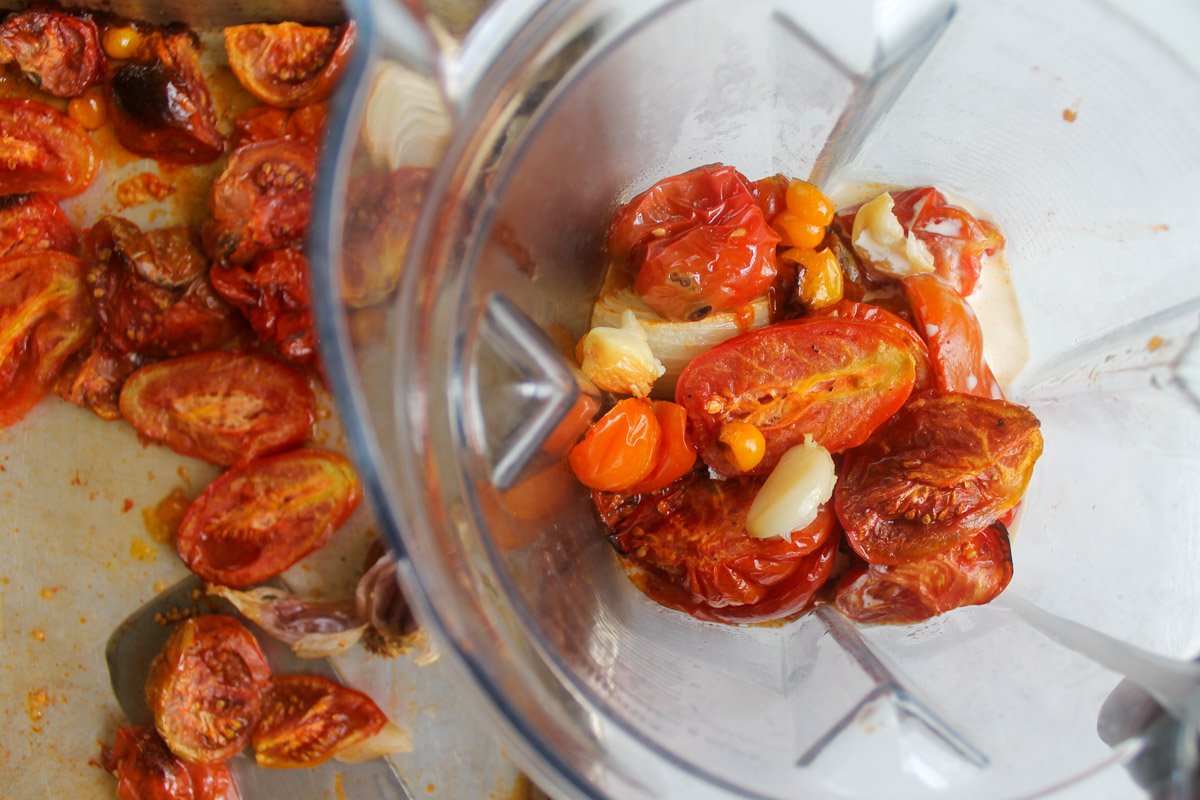 Adding roasted tomatoes, onions and garlic to a blender.