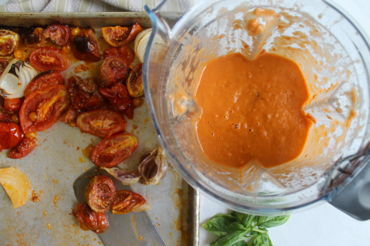 Roasted tomatoes on a sheet pan next to a blender of tomato soup.