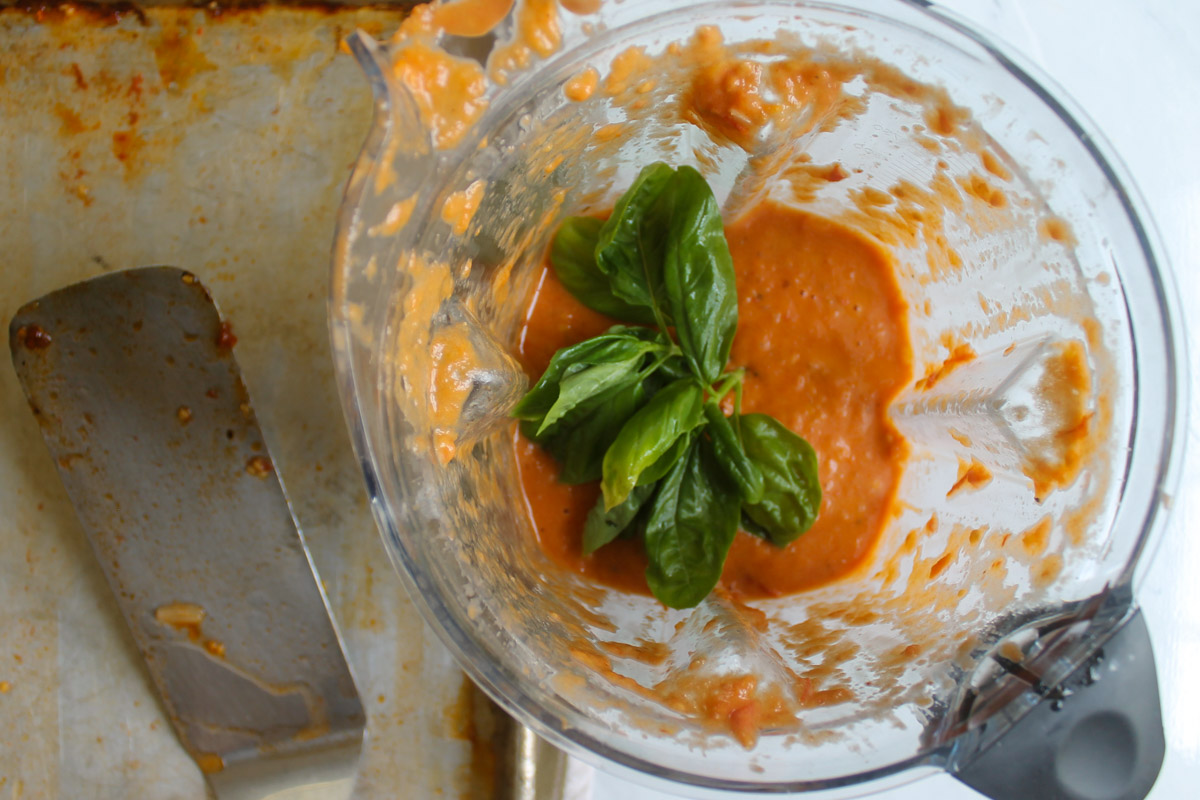 Adding fresh basil to a blender of roasted tomato garlic soup.