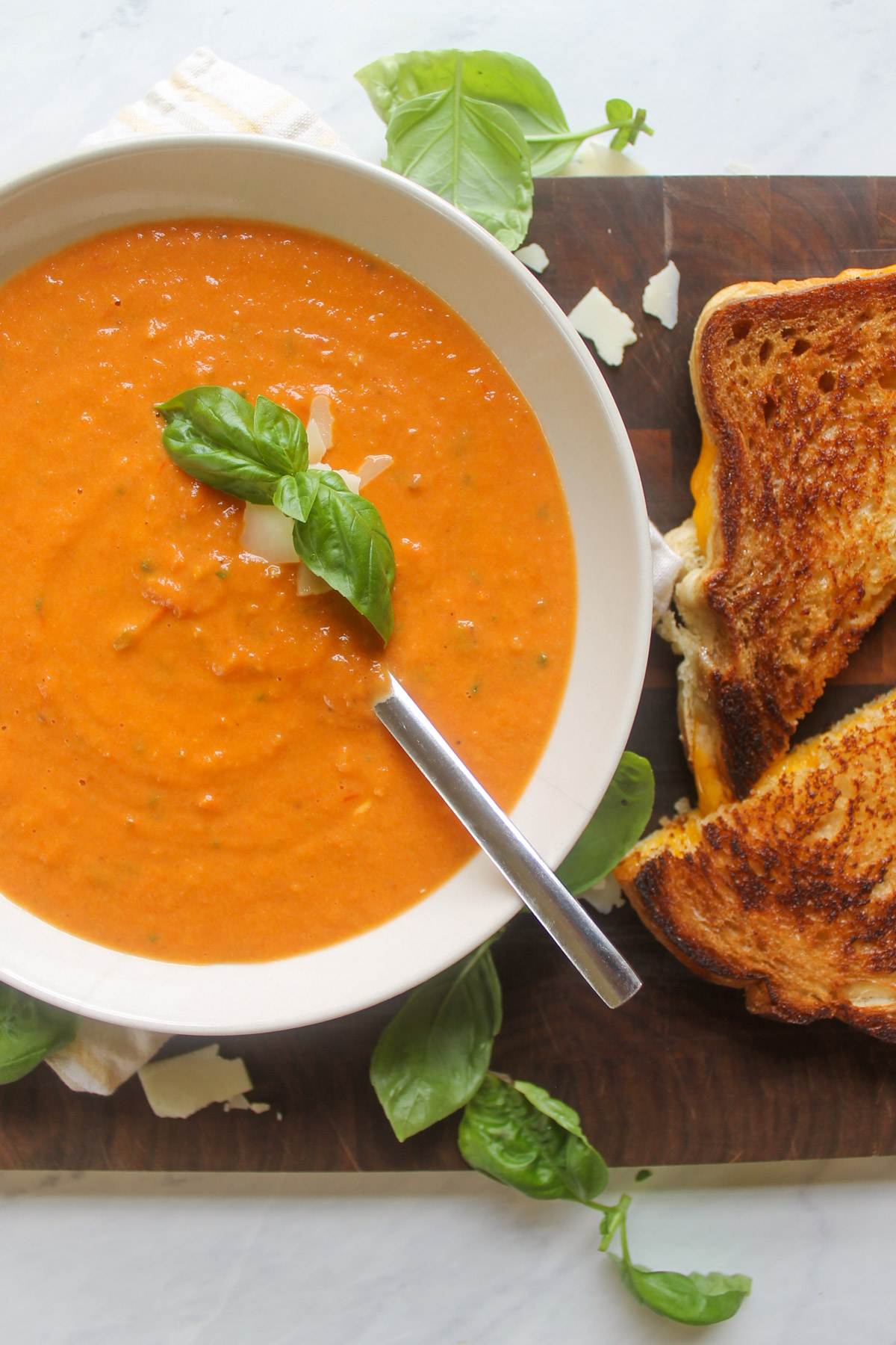 A bowl of tomato soup next to grilled cheese sandwiches for dunking.