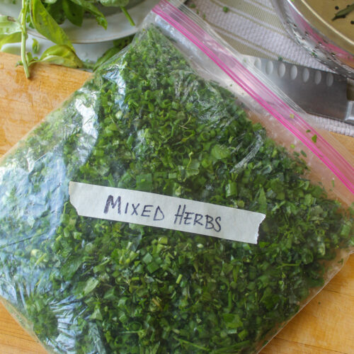 A freezer ziploc bag full of chopped herbs and greens with a masking tape label Mixed Herbs.