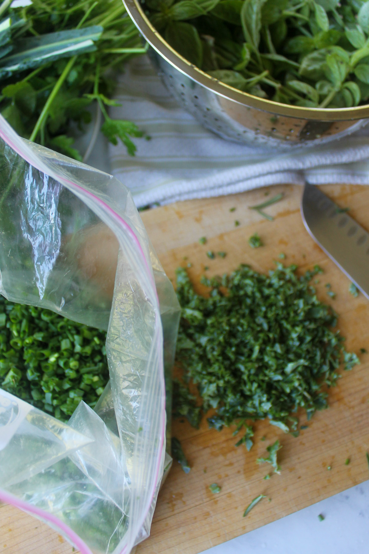 An open freezer bag with chopped herbs in it and some on a cutting board.