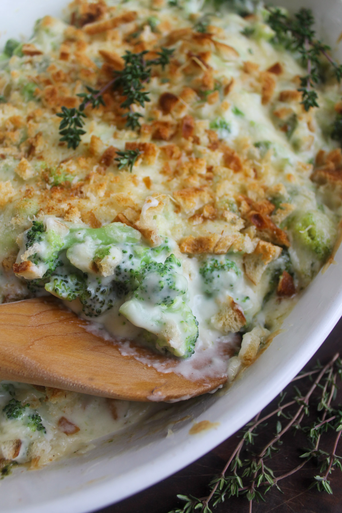 A dish of creamy broccoli au gratin with a wooden spoon serving it.