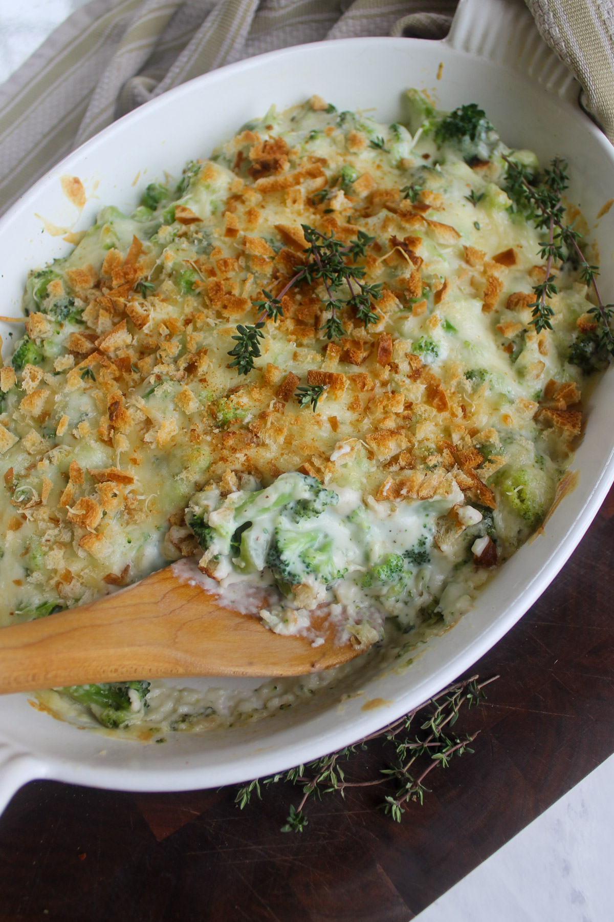 A white oval dish of baked broccoli au gratin with breadcrumbs and fresh thyme.