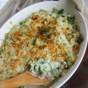 A white baking dish of broccoli au gratin with a wooden spoon.