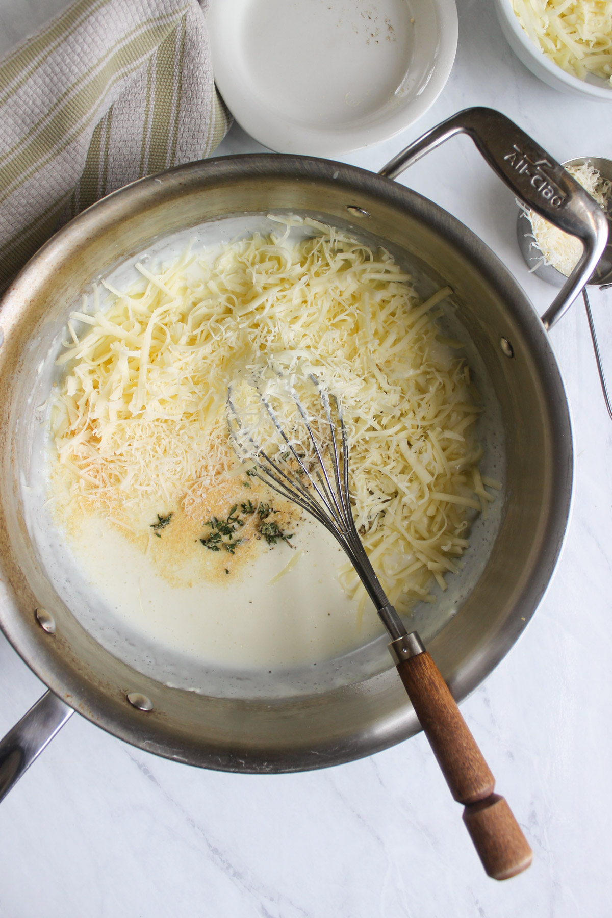 Adding shredded white cheddar cheese and seasonings to a white sauce.