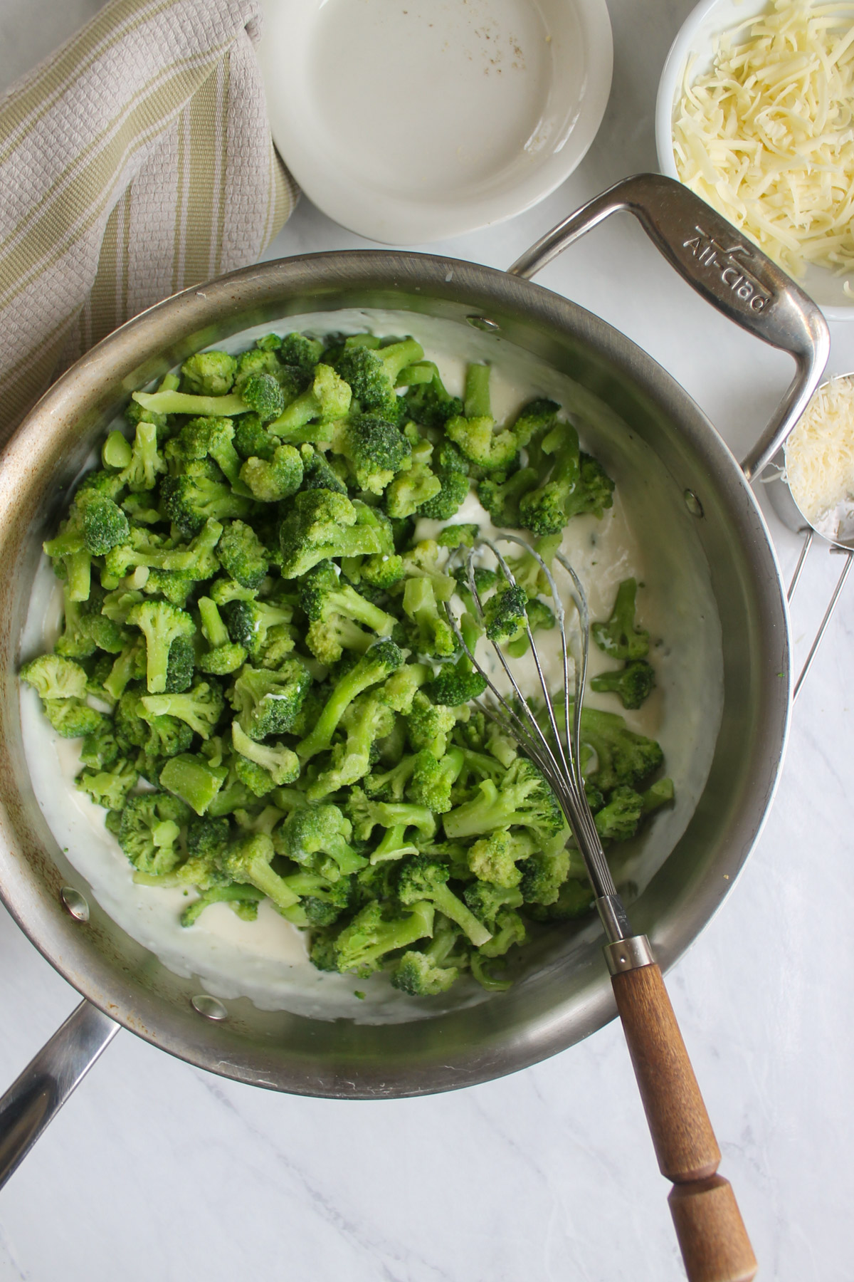 Adding frozen broccoli to a white cream sauce in a skillet.