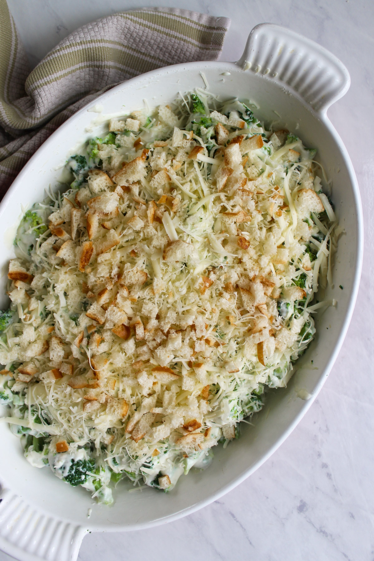 An oval baking dish of broccoli au gratin, unbaked and ready for the oven.