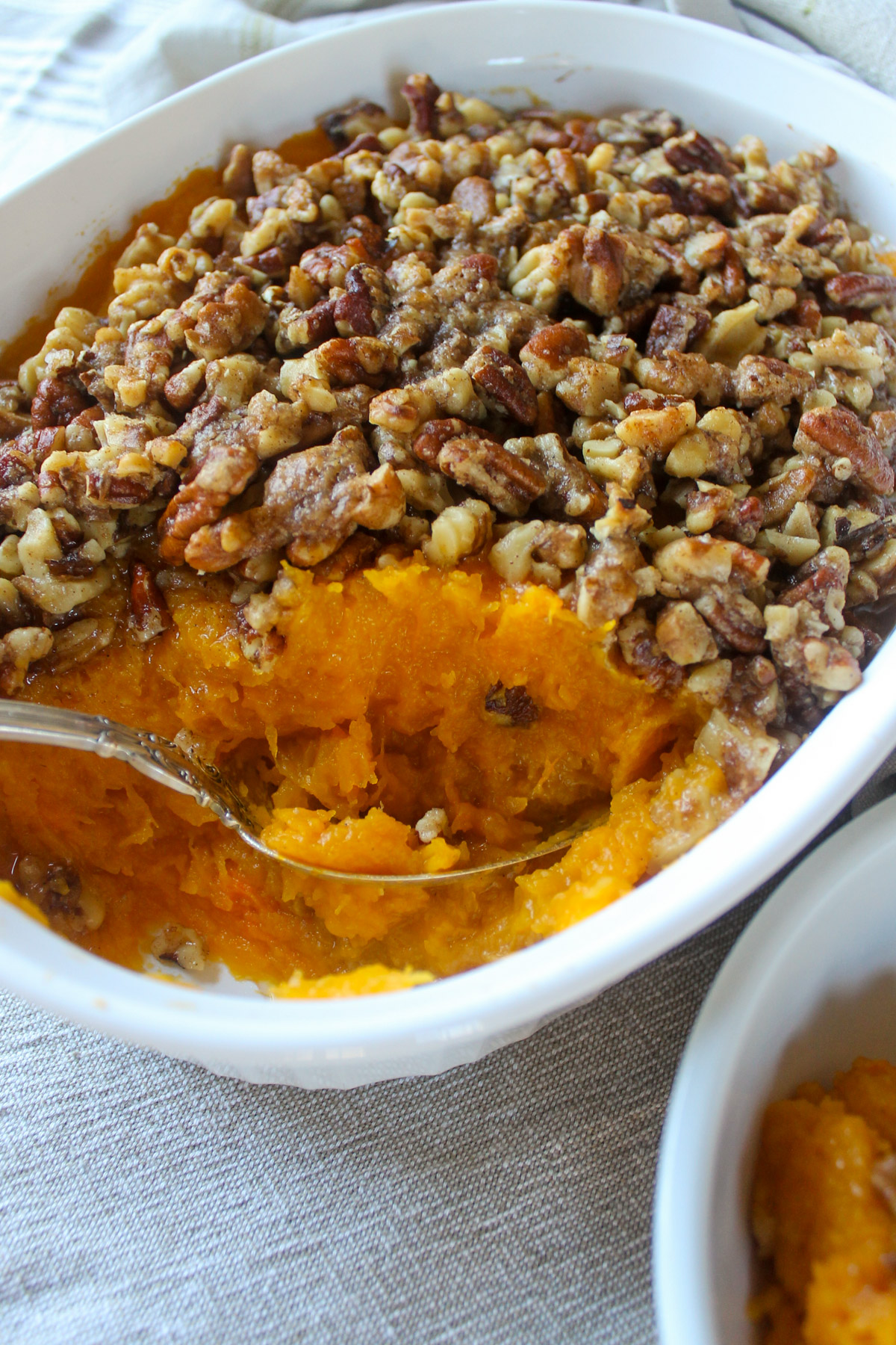 A spoon scooping out orange butternut squash with butter pecan topping.