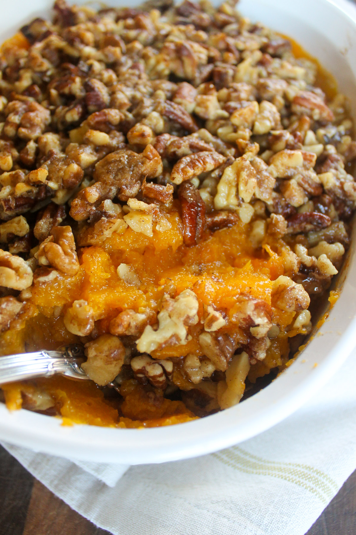 Butternut squash casserole with nut topping being scooped with a spoon.