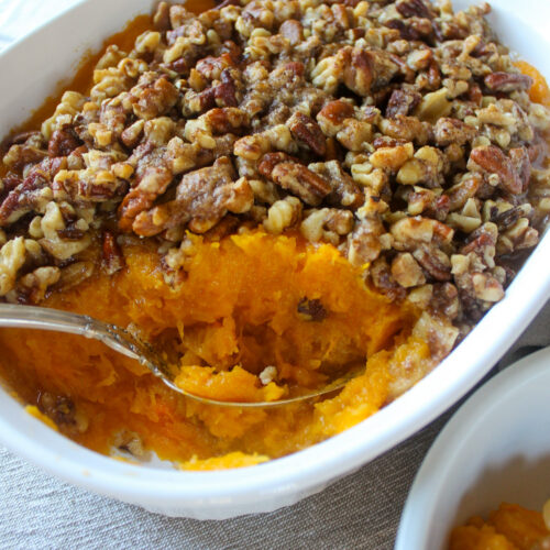 A white baking dish of butternut squash casserole with pecan brown sugar topping.
