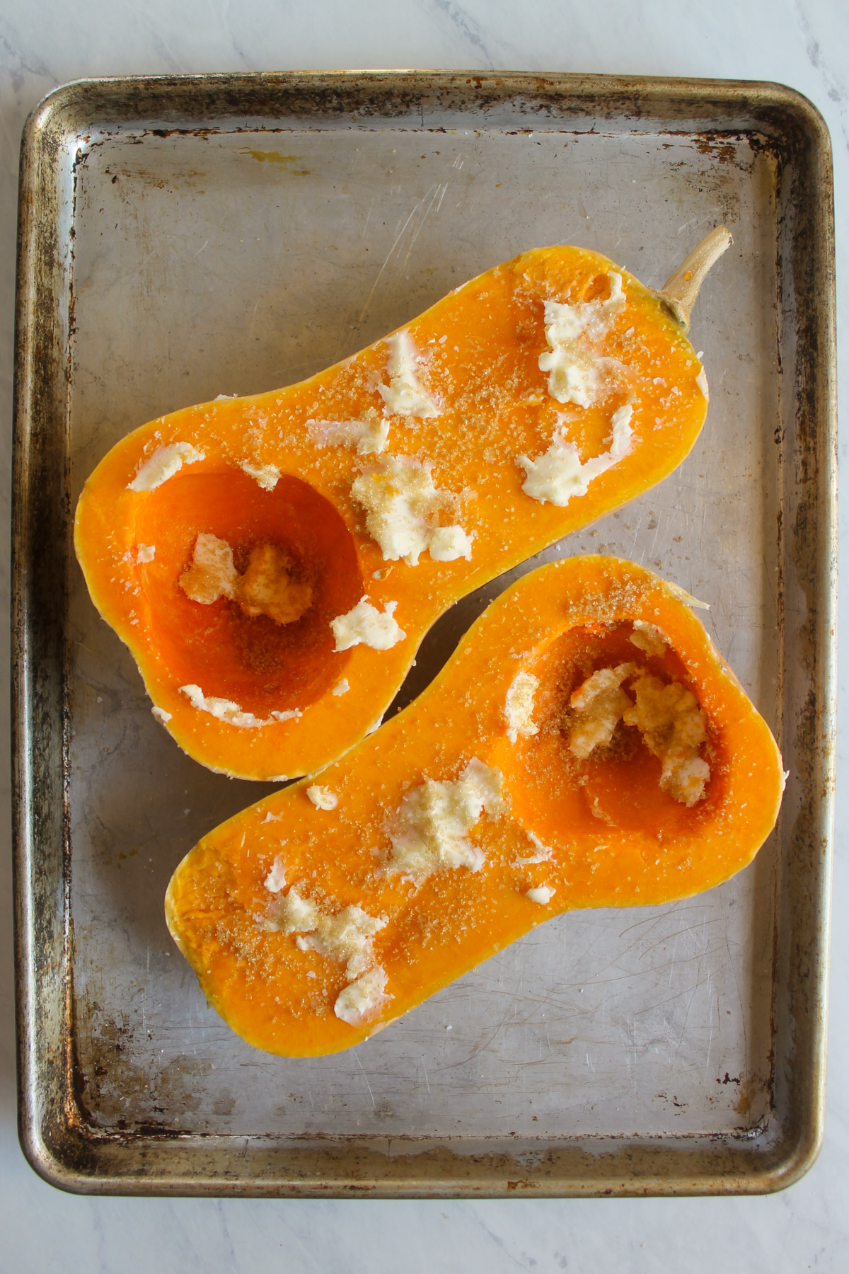 Butternut squash halves on a sheet pan smeared with butter, brown sugar and salt.