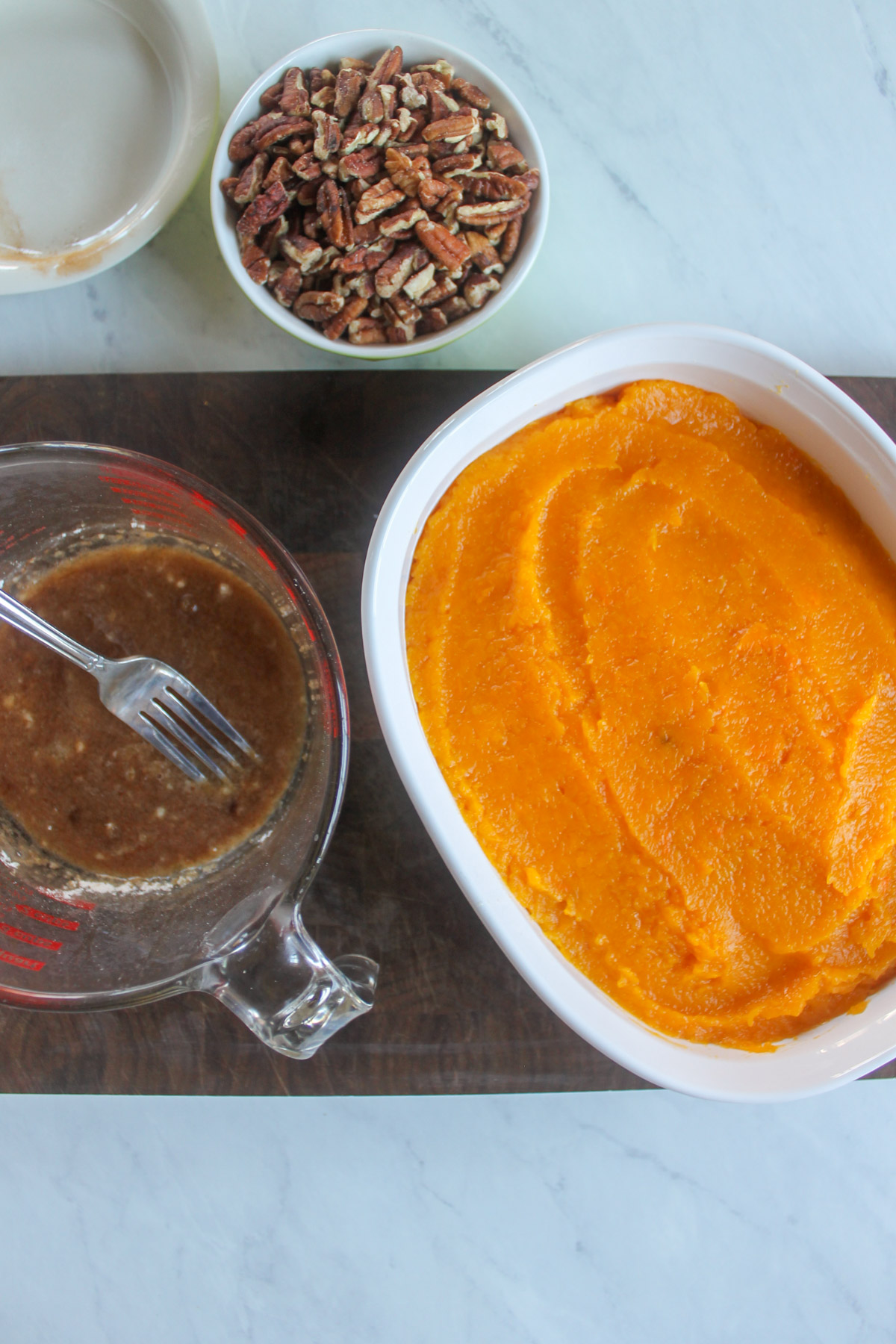 Mashed butternut squash smoothed into a casserole dish with ingredients for the topping.