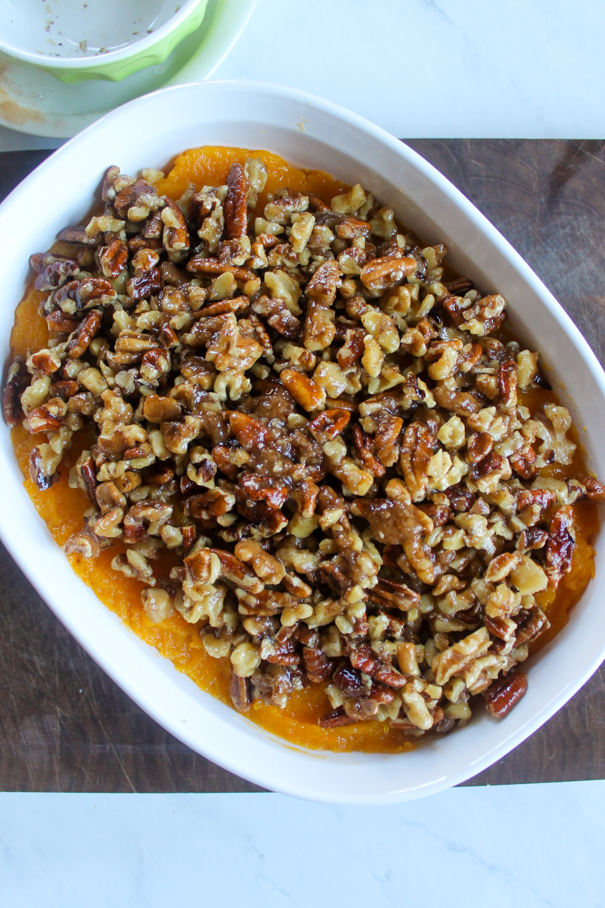 A white baking dish of mashed butternut squash topped with butter pecan topping ready to bake.