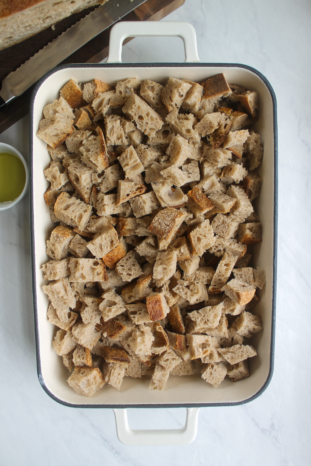A white baking dish full of cubed wheat crusty bread.